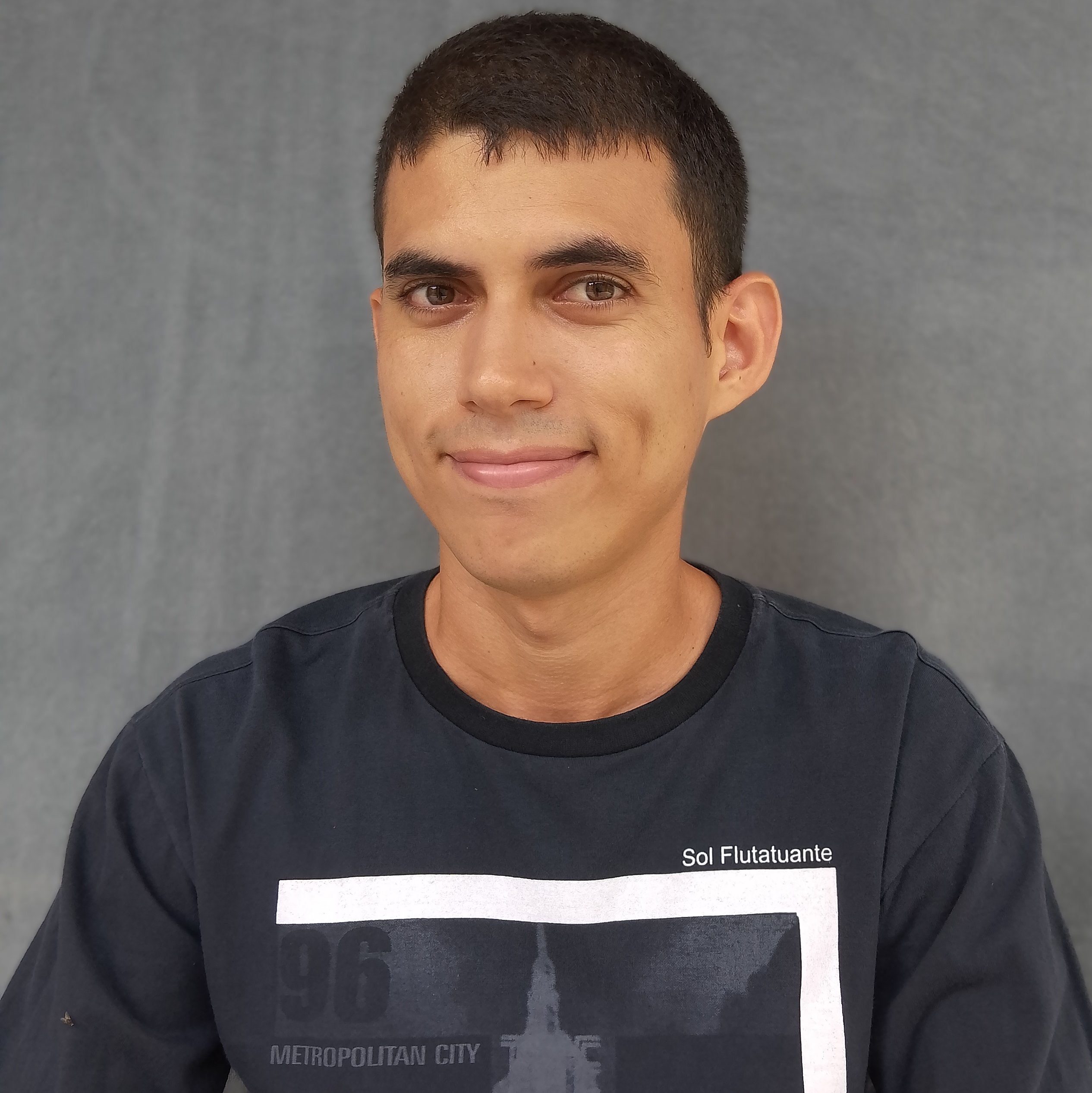 A picture of me (young man with brown eyes and short black hair) smiling, with a gray background, wearing a black shirt.